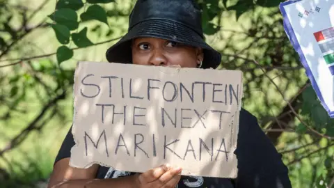 Getty Images A woman in a black sun hat stands with a handmade cardboard placard  that says 