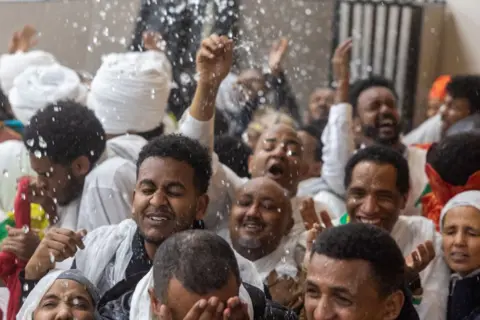 AMID FARAHI / AFP People smile as they are doused with water by clergy at an Ethiopian Orthodox Cathedral.