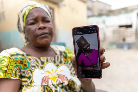 JEROME FAVRE / EPA A grieving woman holds up a smartphone, showing a photo of her daughter smiling and dressed in pink.