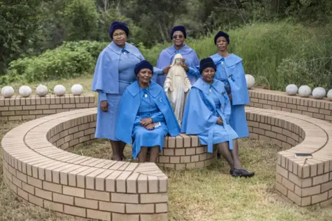 MARCO LONGARI / AFP Women dressed in matching blue clothing stand close to a stone statue.