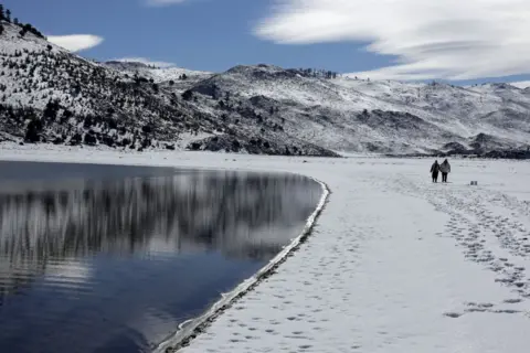 ABDEL MAJID BZIOUAT / AFP People take a stroll in the snow by Lake Sidi Ali. All of the landscape is covered in snow.