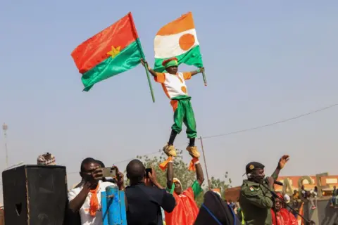 ISSIFOU DJIBO / EPA Men hold a boy up in the air. He is waving the flag of Burkina Faso and the flag of Niger.