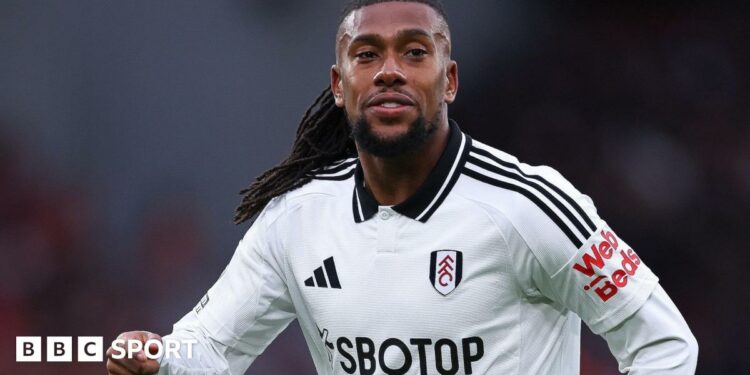 Alex Iwobi, wearing a white Fulham shirt, looks to the right of screen as black dreadlocks are seen over his left shoulder and he raises his right arm to chest height