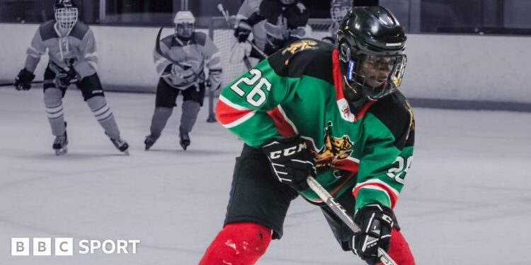 Benjamin Mburu, wearing a green T-shirt, black shorts, rollerblades and black ice hockey gloves, holds a stick and tries to control a puck on a tiled floor in his house