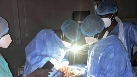 Mudathir Ibrahim Suleiman Doctors in el-Fasher's Saudi Hospital performing a caesarean using light from mobile phones