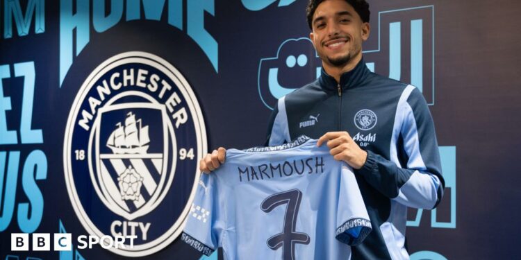 Omar Marmoush holding a Manchester City shirt with the number seven on the back