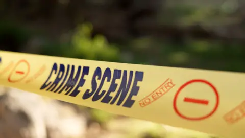 Getty Images A generic crime scene - no entry sign is seen in front of a blurred background. The yellow and blue tape is restricting entry to an active scene being investigated by police.