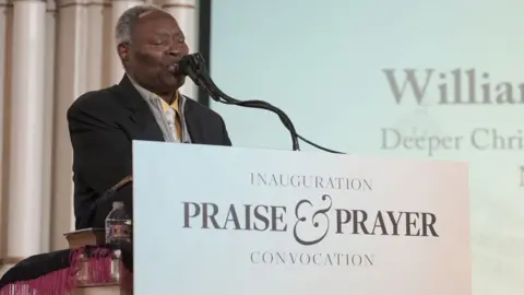 Global Crusade with Kumuyi/Kevin Smart Media William Kumuyi standing at a pulpit behind a sign that says 