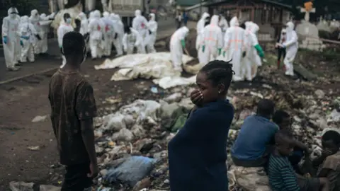 AFP Youngsters in Goma watch as undertakers in white protective gear surround similarly white body bags