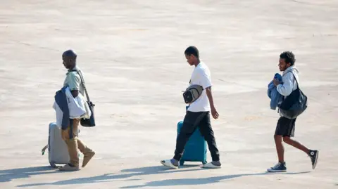 Thai News Pix Three people released from scam centres walk across a tarmac