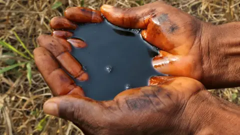 Getty Images A man holds a pool of black oil in the palm of their hands in Ogoniland, Nigeria